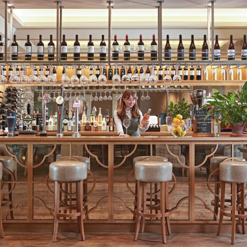 Bar staff behind bar smiling with bottle